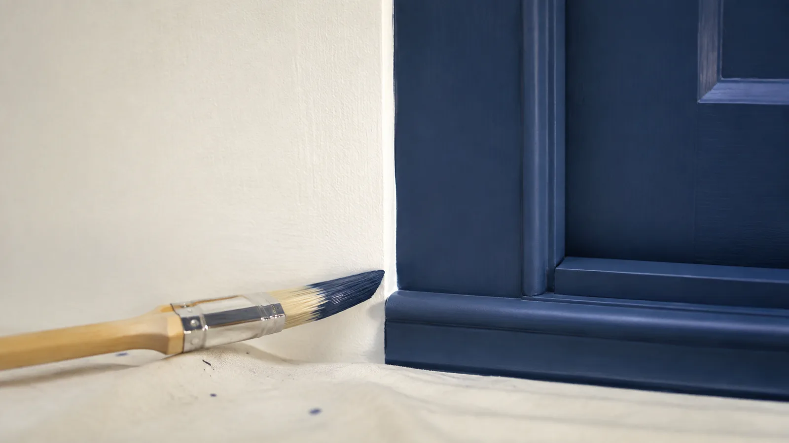 AI-generated illustration: Close-up clean cream wall meeting deep blue door trim, a plain angled brush resting on protected sill, emphasis on precise edge.
