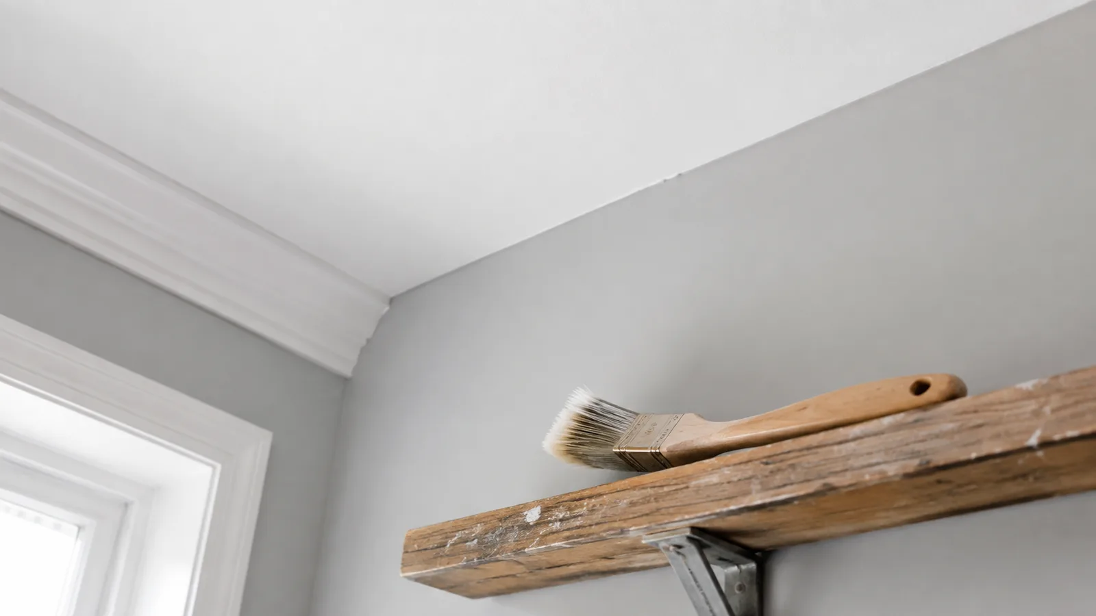 AI-generated illustration: Upward view of a neat wall-ceiling junction, pale gray wall white ceiling and an unbranded angled sash brush resting on a safe shelf below.
