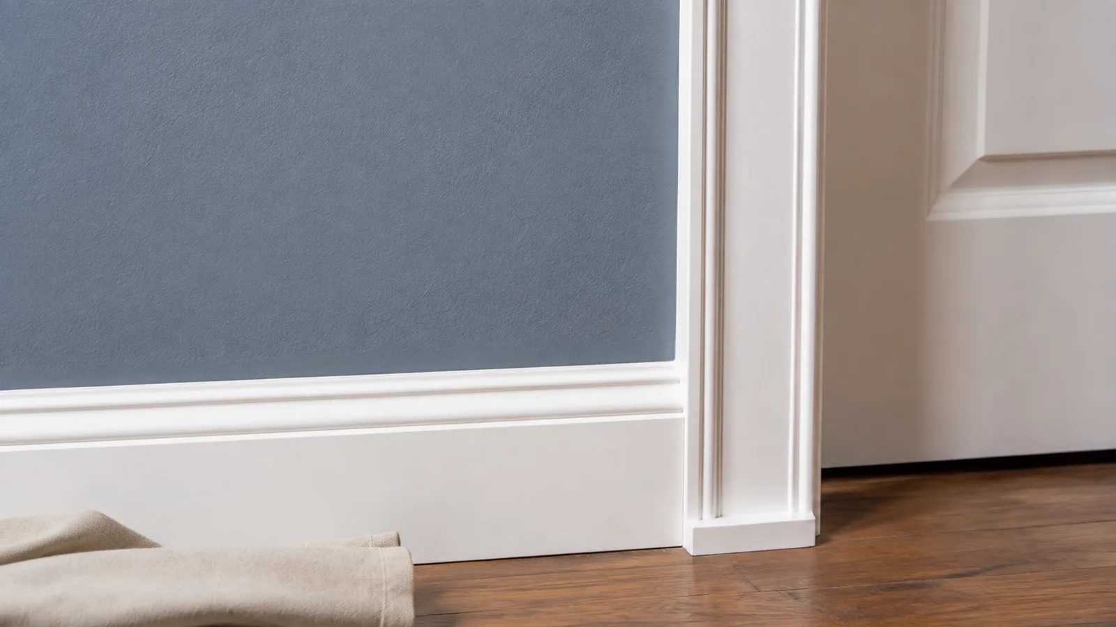 AI-generated illustration: A close architectural detail of a crisp white door casing against a muted blue painted wall, sharp clean paint boundary, natural daylight across the texture, small folded canvas cloth at floor level